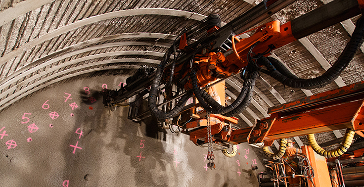 An underground drill jumbo is an example of percussive drilling. The first mechanized percussive drill was invented in 1844 using compressed air to apply the percussive load to strike the drill. Photo: AcademyBlasting.com