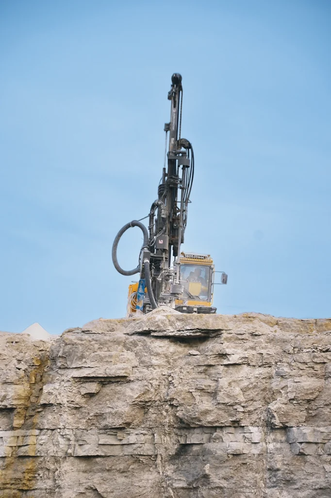 Photo of a track-mounted drill rig at work on a quarry bench.