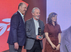 McLanahan Corp.’s Mark Krause (center) is the 2026 recipient of the Barry K. Wendt Memorial Commitment Award. Wirtgen America’s Craig Lamarque (left) and Kristi Wendt, daughter of the late Barry Wendt, stand with Krause during the award presentation. (Photo: P&Q Staff)