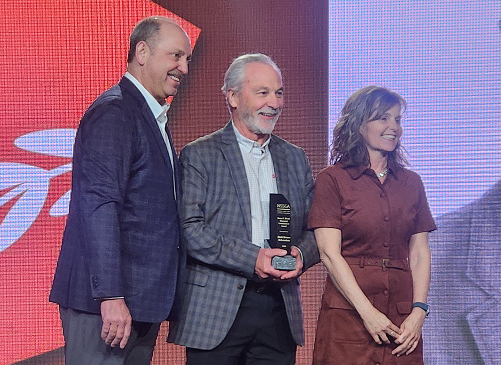 McLanahan Corp.’s Mark Krause (center) is the 2026 recipient of the Barry K. Wendt Memorial Commitment Award. Wirtgen America’s Craig Lamarque (left) and Kristi Wendt, daughter of the late Barry Wendt, stand with Krause during the award presentation. (Photo: P&Q Staff)